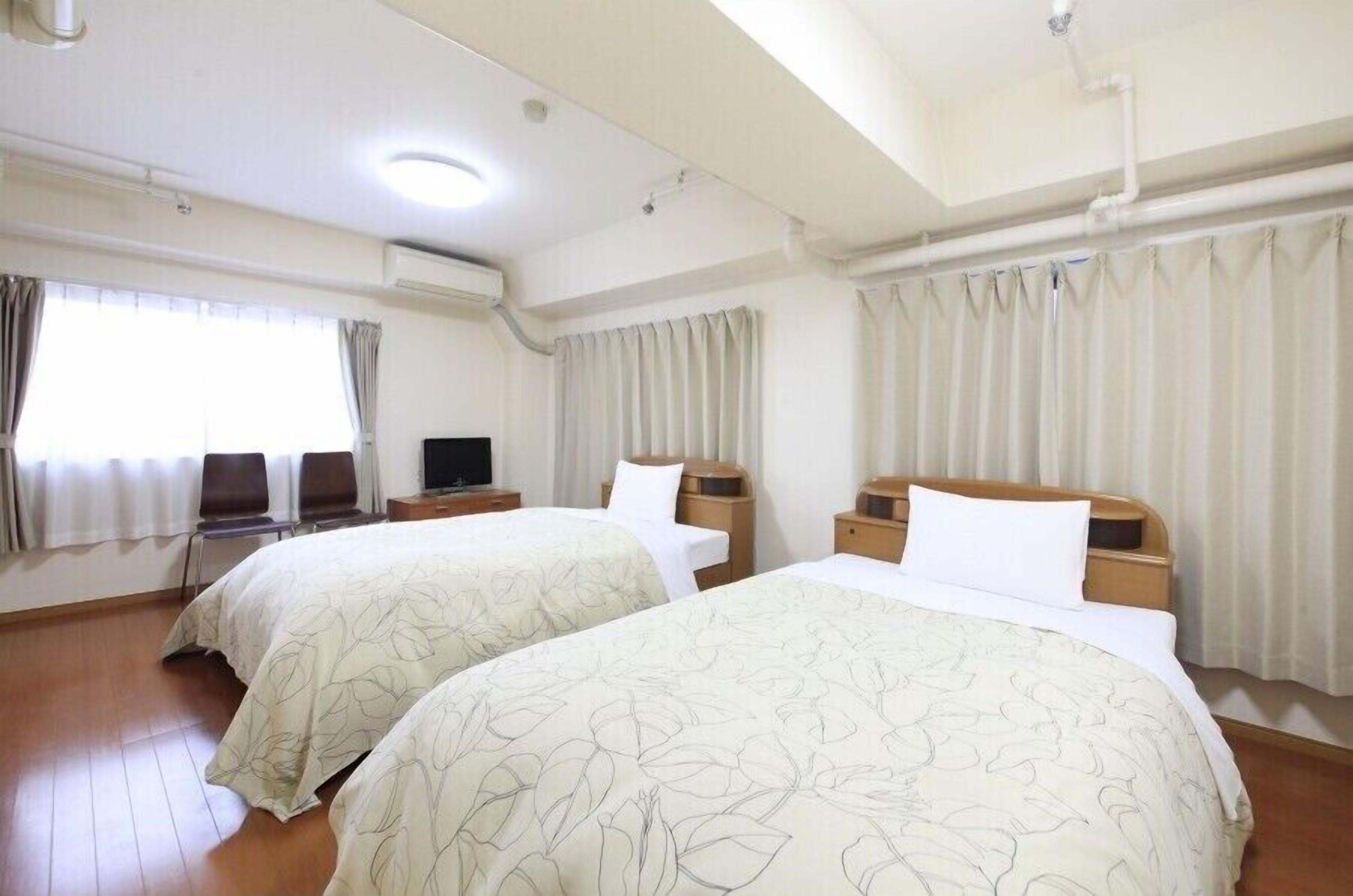 A hotel room with two beds, a desk, a chair, and a television.