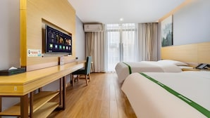 A hotel room with a wooden desk, a flat-screen TV, a bed with a green bedspread, and a large window with curtains. - Greentree Inn Anqing Duxiu Avenue Greenland Metrop (Anqing)
