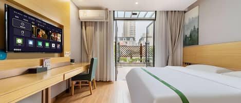 A hotel room with a bed, a desk with a computer, a TV, and a view of buildings through the window.