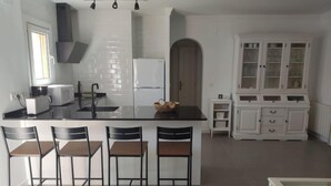 Eine moderne Küche mit Kochinsel, Barhocker, einem weißen Schrank mit Glastüren und einem kleinen Esstisch.