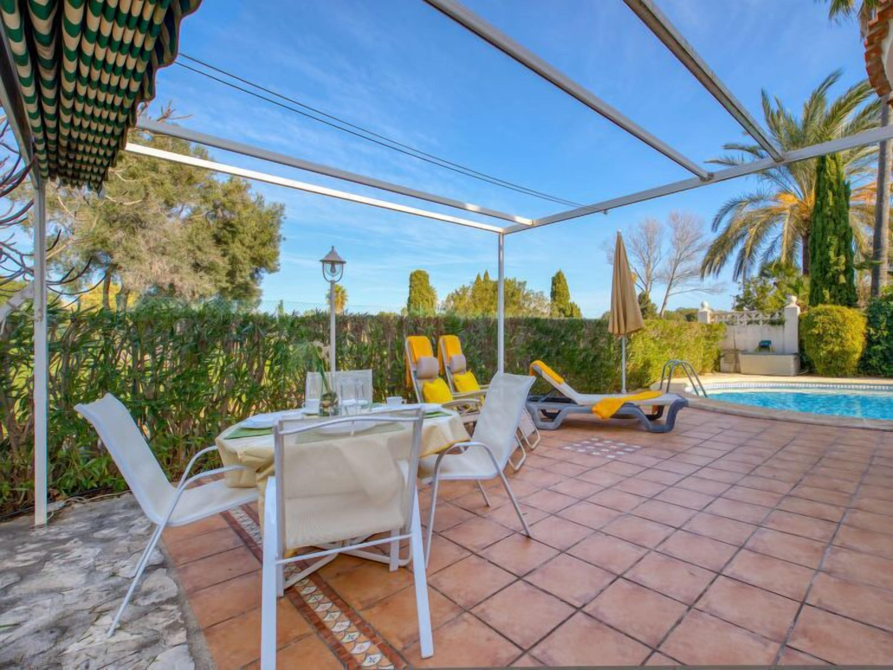 An outdoor patio with a pool, covered seating area, and a table with chairs.