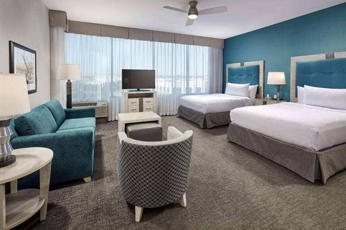 A hotel room with two beds, a sofa, a small table, a TV, and a window with curtains.