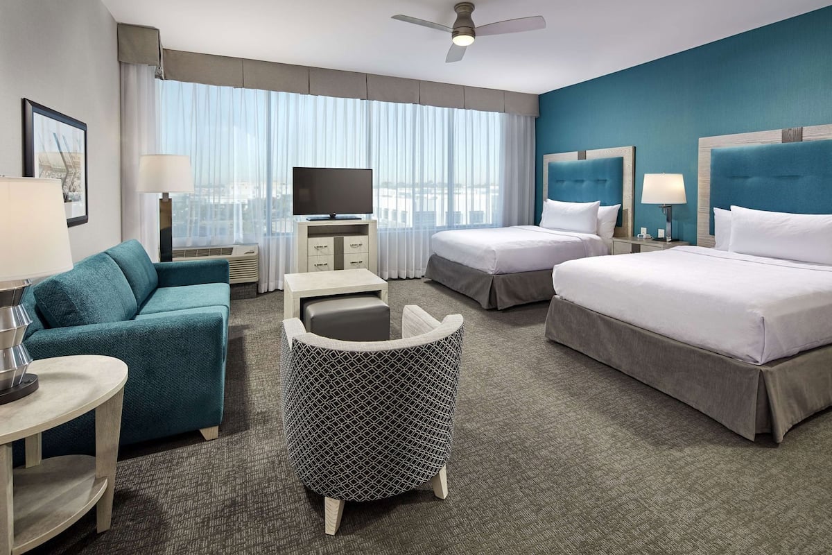 A hotel room with a sofa, two beds, a TV, a desk, and a chair.