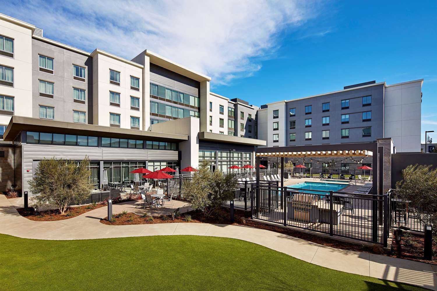 A modern hotel with a pool area, outdoor seating, and a well-maintained lawn.