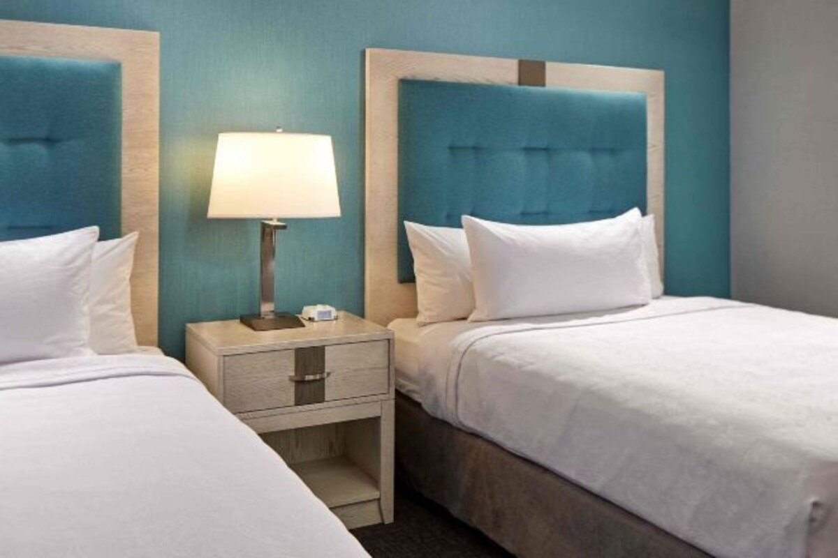 A hotel room with two beds, each with a headboard, a bedside table with a lamp, and a small drawer.