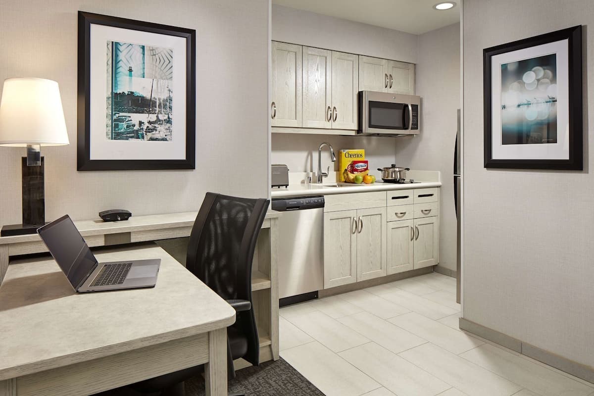 A modern kitchen with a microwave, refrigerator, and a dining area with a laptop on the table.