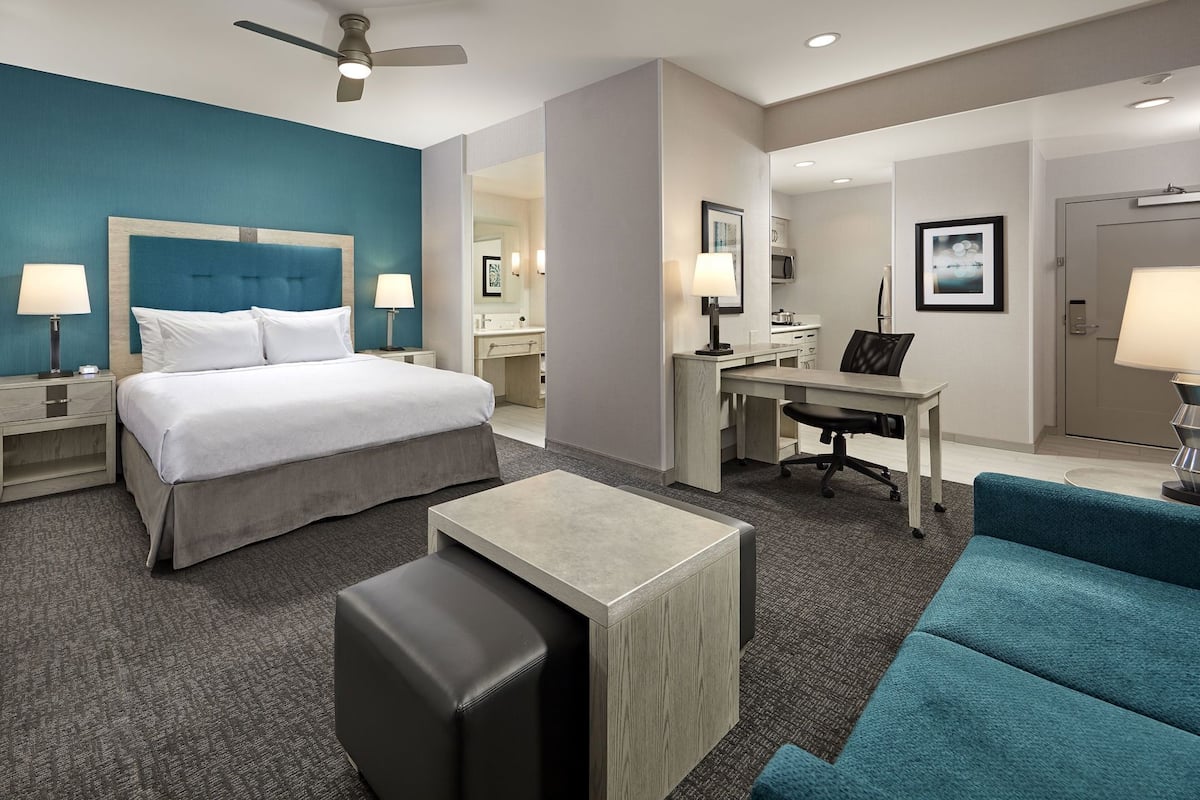 A hotel room with a bed, desk, chair, and a blue sofa.