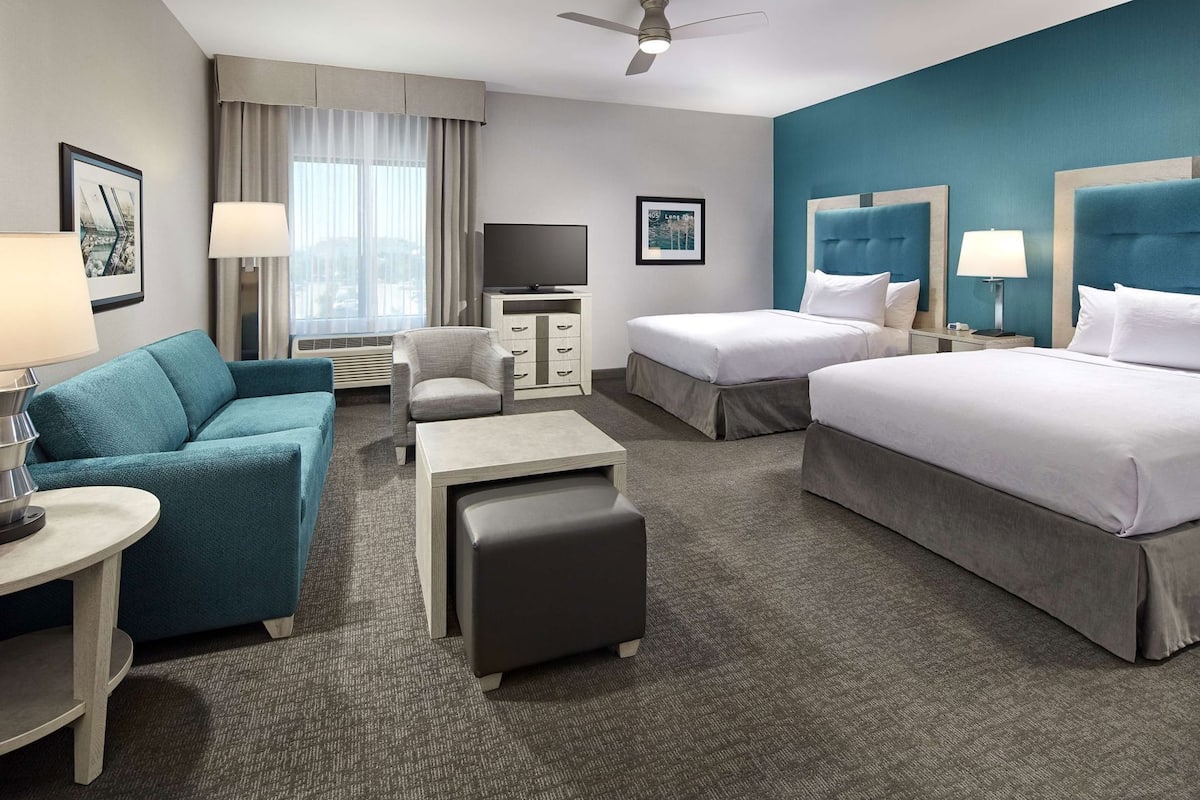 A hotel room with a sofa, two beds, a TV, a desk, and a chair.