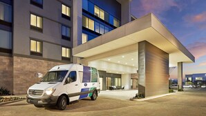 A modern hotel entrance with a white van parked in front, a covered outdoor area, and a multi-story building with large windows. - Homewood Suites by Hilton Long Beach Airport (Long Beach)