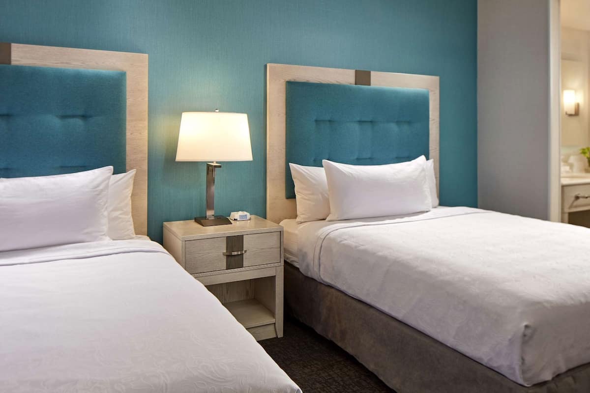 A hotel room with two beds, a nightstand with a lamp, and a mirror.