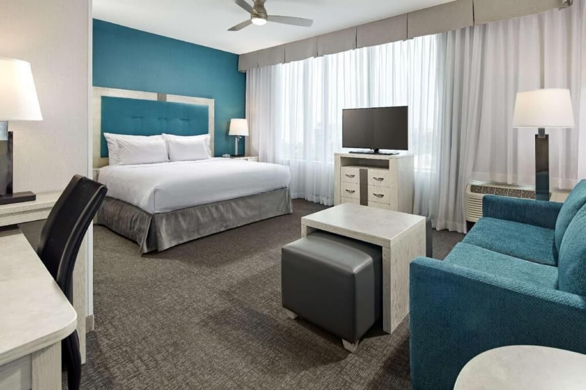 A hotel room with a bed, a desk, a chair, a TV, and a ceiling fan.