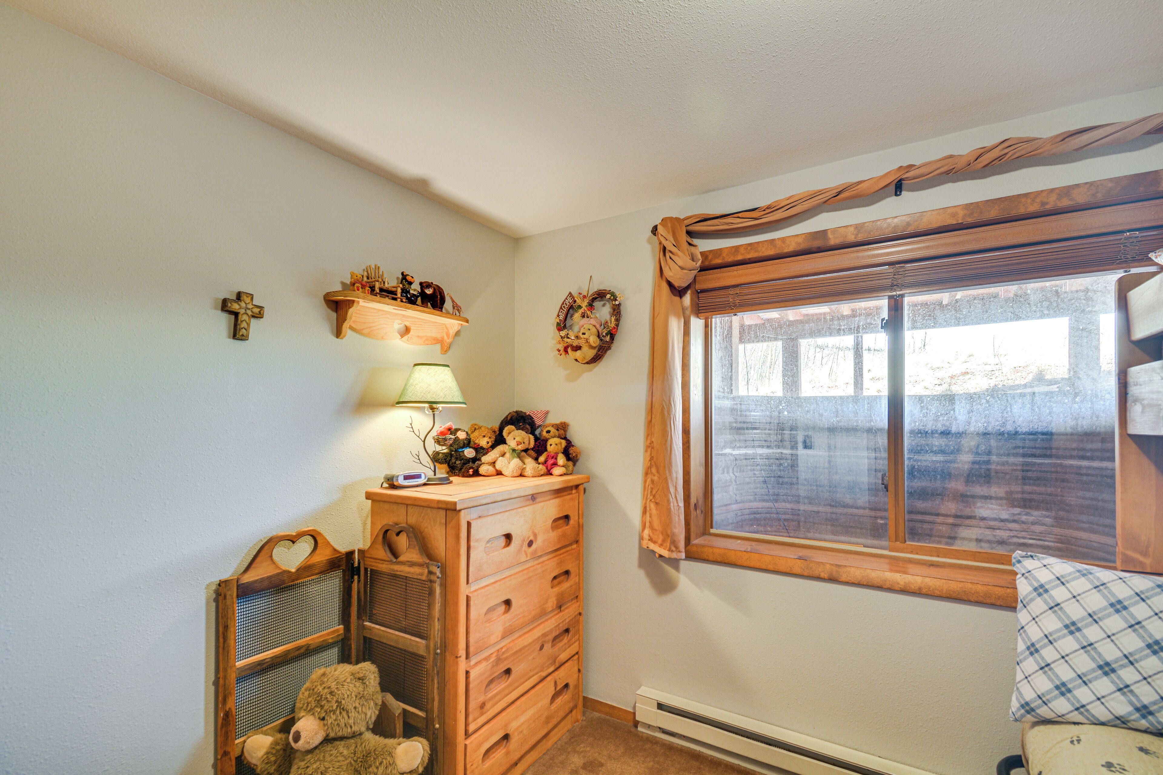 Une pièce avec une commode en bois, une fenêtre avec des rideaux, un ours en peluche et des décorations murales.
