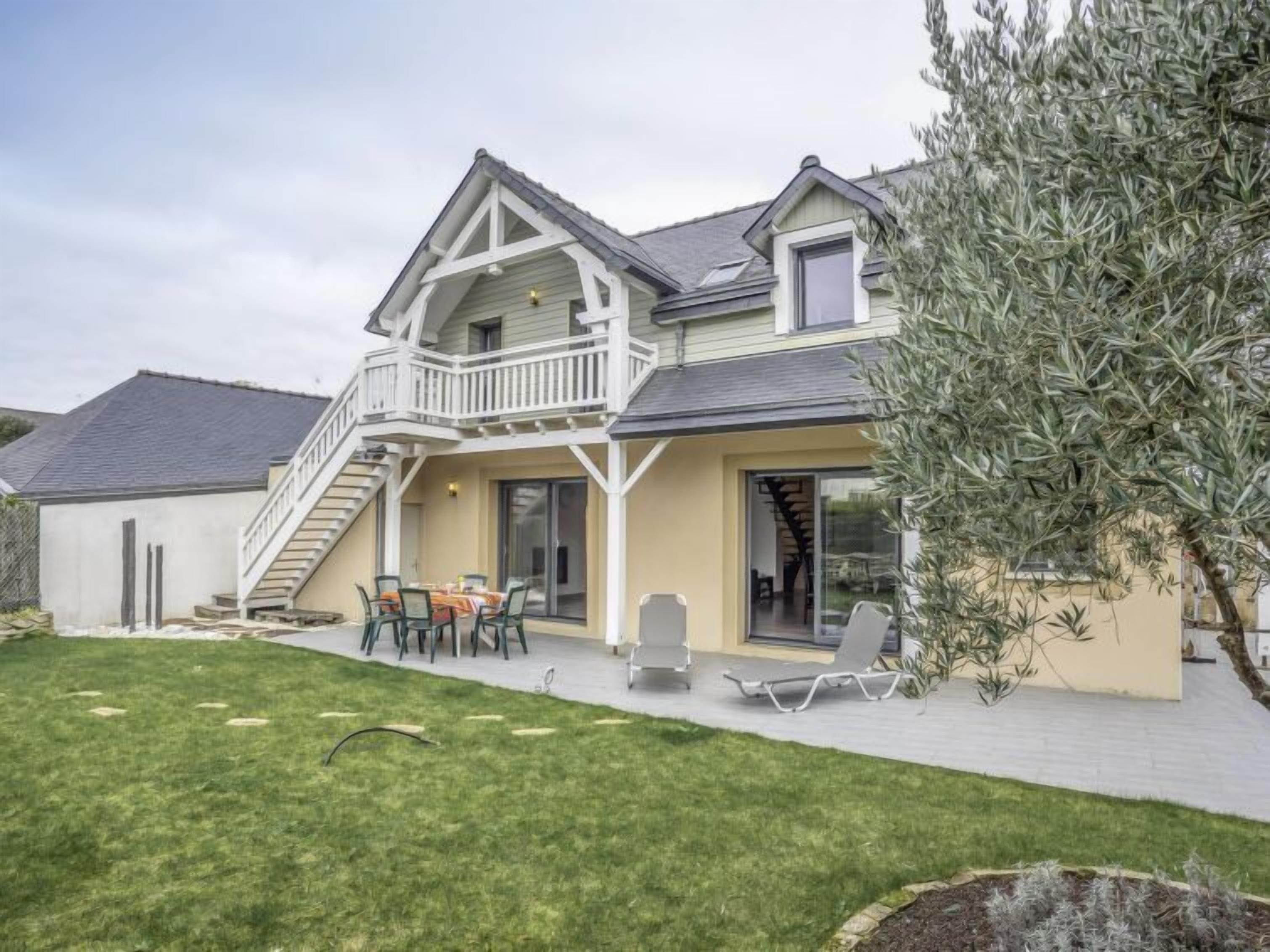 A two-story house with a balcony, a patio with outdoor furniture, and a well-maintained lawn.