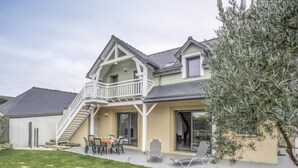 Una casa de dos pisos con balcón, un patio con mobiliario exterior y un césped bien cuidado.