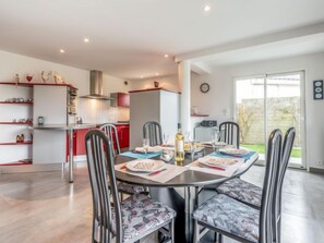 A modern kitchen with red cabinets, a dining area with a round table and chairs, and a large sliding glass door leading to a backyard.