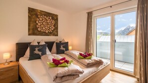 Un dormitorio con cama, mesita de noche, una obra de arte en la pared y un ventanal con cortinas.