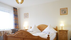 Un lit en bois avec une literie blanche, deux tables de chevet avec des lampes, une chaise et une fenêtre avec des rideaux.