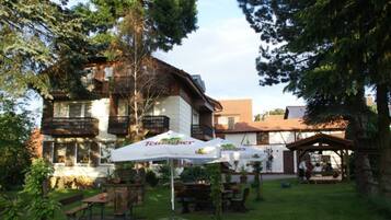 A building with outdoor seating and umbrellas, surrounded by trees.