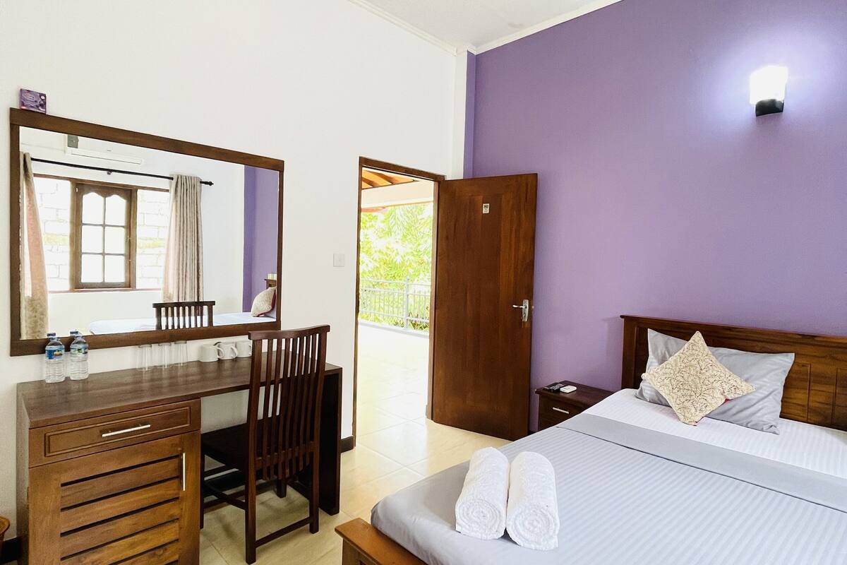 A bedroom with a bed, a wooden desk, a chair, a wardrobe, and a ceiling fan.