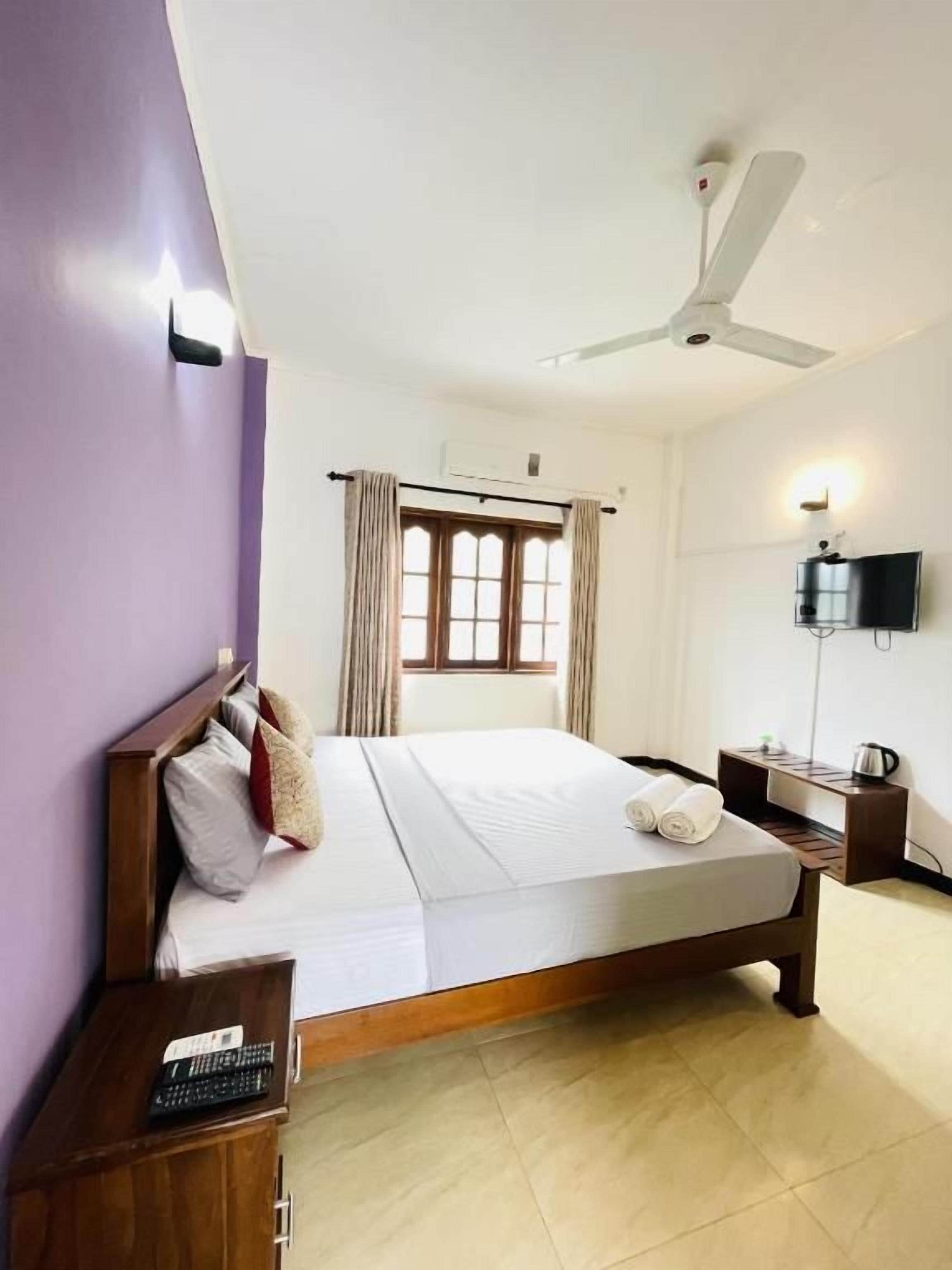 A hotel room with a bed, a ceiling fan, a TV, and a window with curtains.
