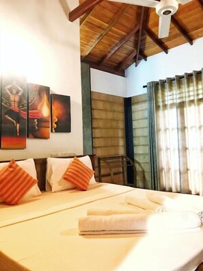 Una habitación de hotel con una cama, almohadas, un ventilador de techo y una obra de arte en la pared.