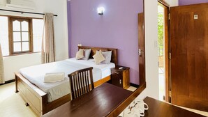 A bedroom with a bed, a wooden table with water bottles, a chair, a nightstand, and a ceiling fan. - Ravan Tangalle (Tangalle)