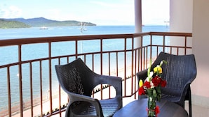 A balcony with two wicker chairs and a table, overlooking a calm sea with a distant island and a ship. - The Shelter Hotel - Port Blair (Port Blair)