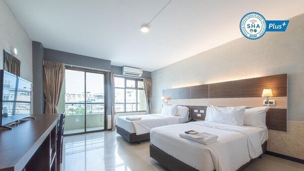 A hotel room with two beds, a desk, a TV, and a large window with curtains. - Ratchaphruek Pavilion (Nakhon Pathom)