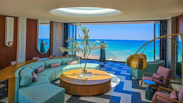 Un salon moderne avec un canapé aux lignes courbes, une table basse ronde et une vue sur l’océan.