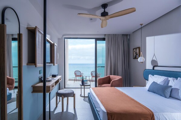 A modern hotel room with a large bed, a desk, a chair, and a balcony with a view of the sea.