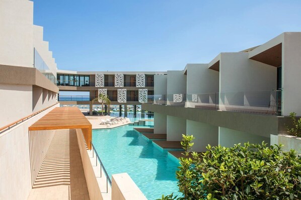 A modern hotel with a central swimming pool, multiple balconies, and a clear sky.