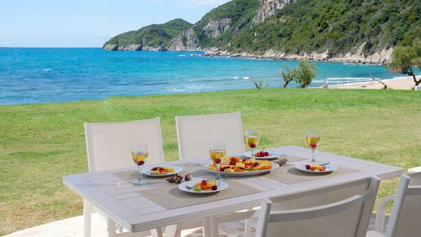Mesa para dos con platos de fruta y copas de vino, con vistas a un paisaje costero con acantilados y el mar.