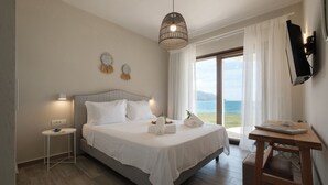 Un dormitorio con cama, mesitas de noche, escritorio y vistas al mar.