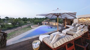 A poolside area with lounge chairs, a wooden deck, and a stone wall.