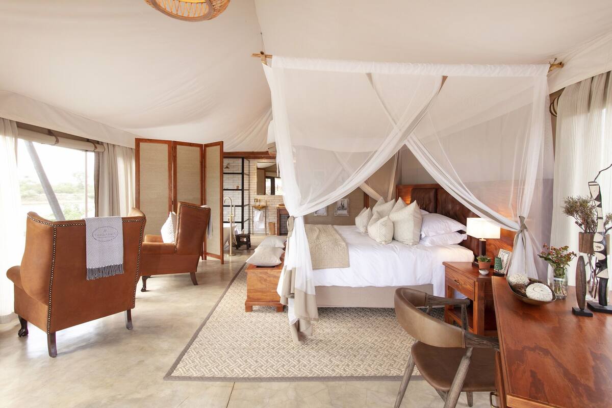 A spacious bedroom with a large bed, a sitting area with a chair, and a bedside table with a lamp and decorative items.