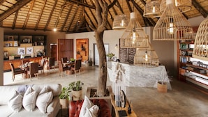 A spacious room with a high ceiling and exposed wooden beams, a dining area with a wooden table and chairs, and a seating area with a sofa and cushions.