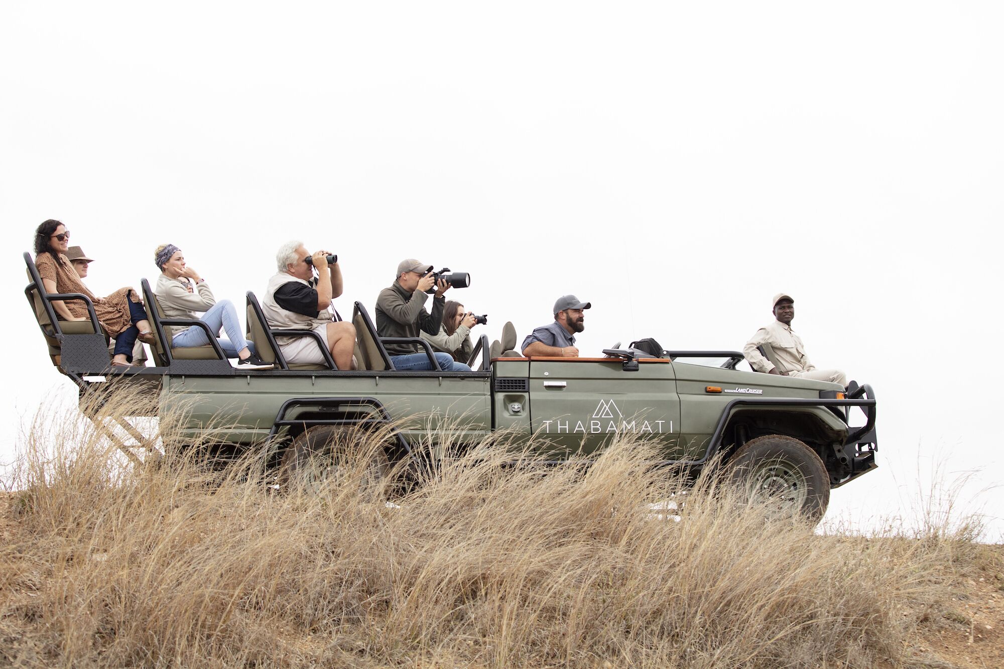 Un vehículo safari con pasajeros, incluido un guía, en un campo de hierba.