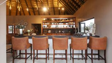 A bar area with a wooden ceiling, bar stools, and a shelf with various bottles and glasses.