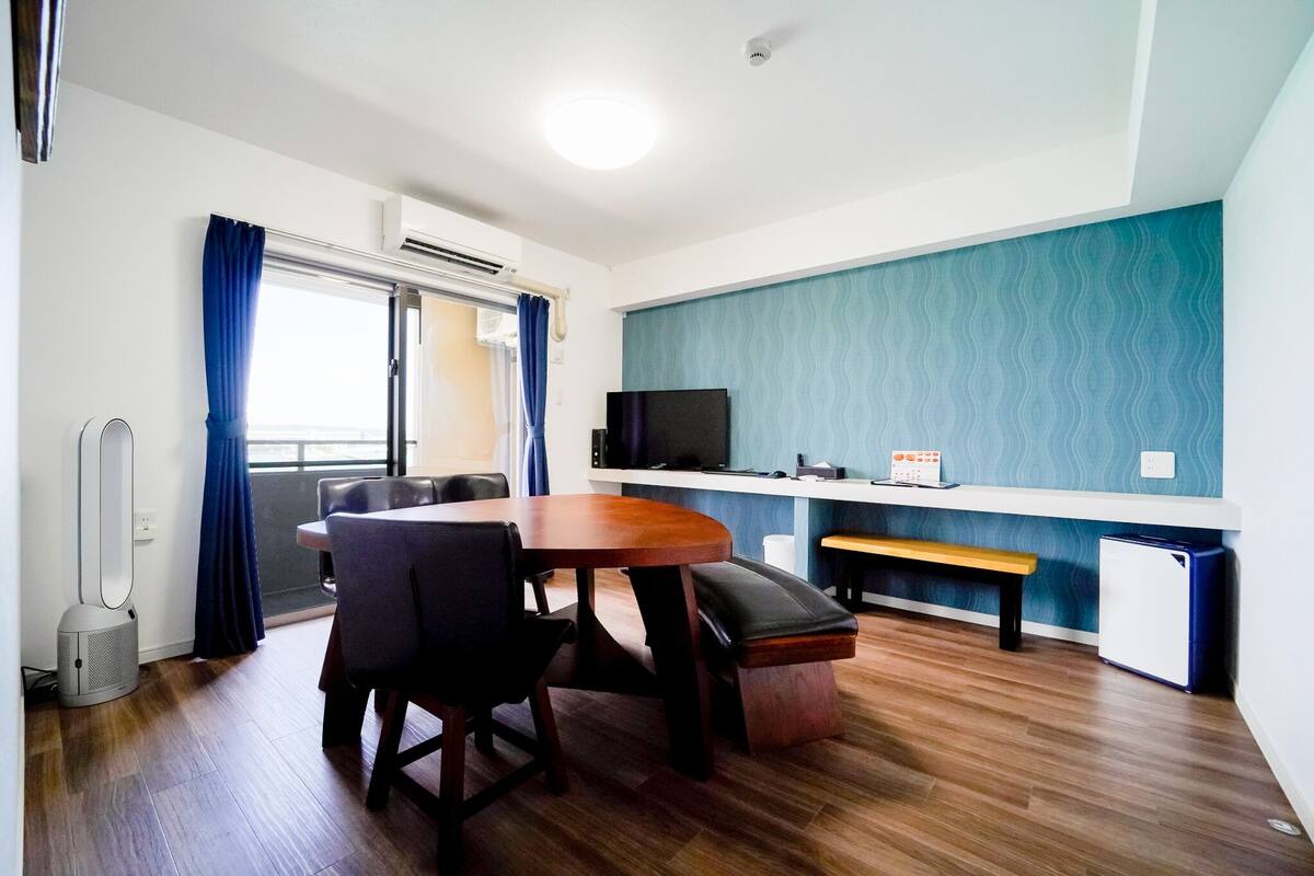 A compact living space with a dining table, chairs, a bench, a TV, and a small refrigerator.