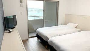 A hotel room with a TV, two beds, a sliding glass door to a balcony, and an air conditioning unit. - Villa Awase 111 (Okinawa)