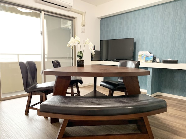 A modern dining area with a round table, black leather chairs, and a flat-screen TV on a wall.