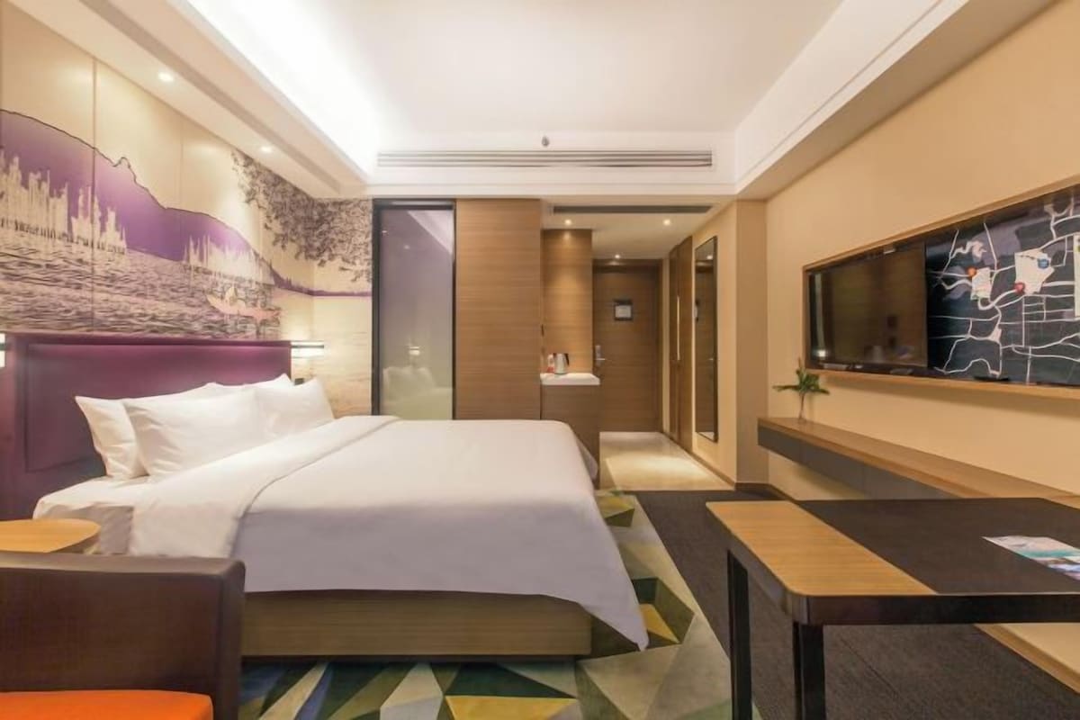 A hotel room with a bed, a desk, a television, and a mural on the wall.