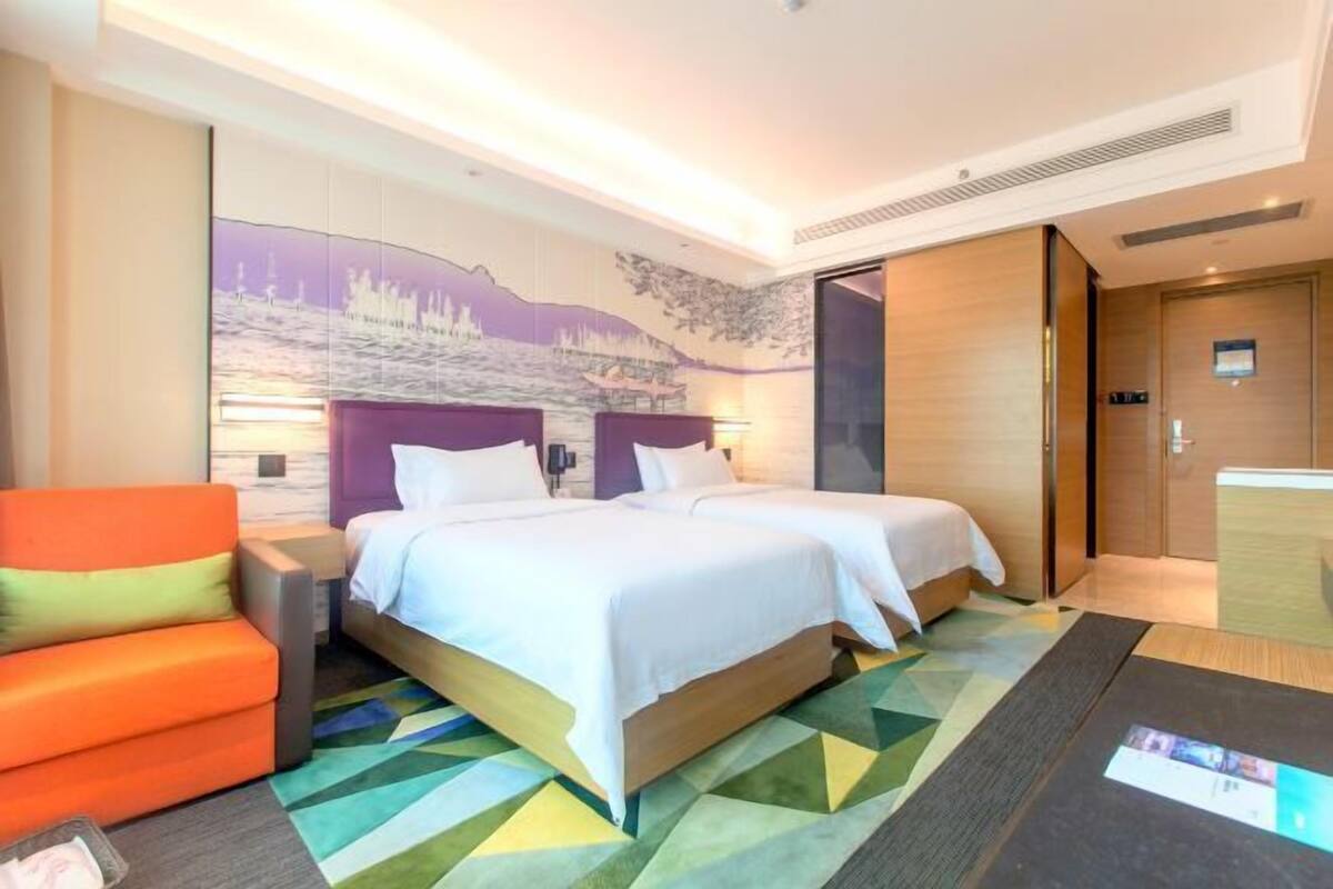 A hotel room with two beds, a sofa, a wall mural, and a wooden door.