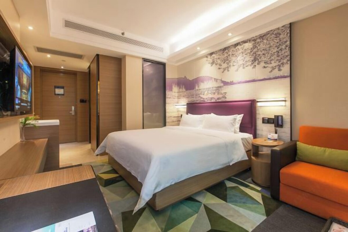 Una habitación de hotel con cama, escritorio, silla, televisor y un muro con estampado floral.