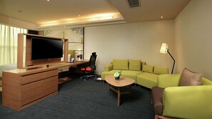 A hotel room with a TV, wooden desk, green sofa, and a small coffee table. - Hampton by Hilton Wuhan Tianhe Airport East (Wuhan)