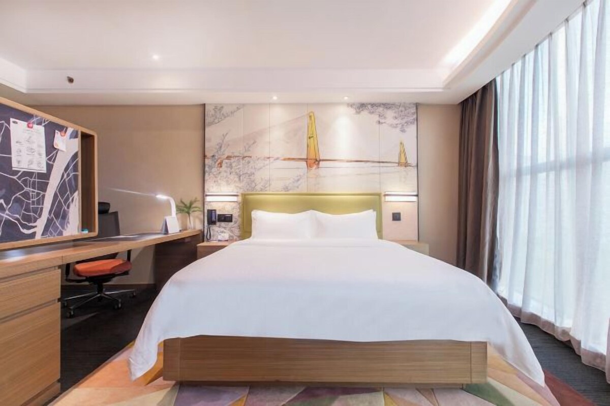 Una habitación de hotel con una cama grande, un escritorio con silla, una mesita de noche y una pared con un mapa y obras de arte.