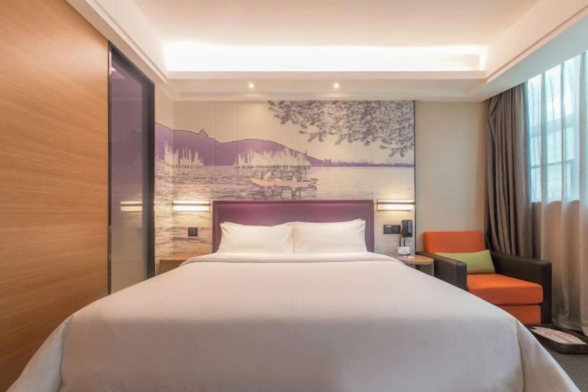 A hotel room with a large bed, a nightstand, a chair, and a mural on the wall.