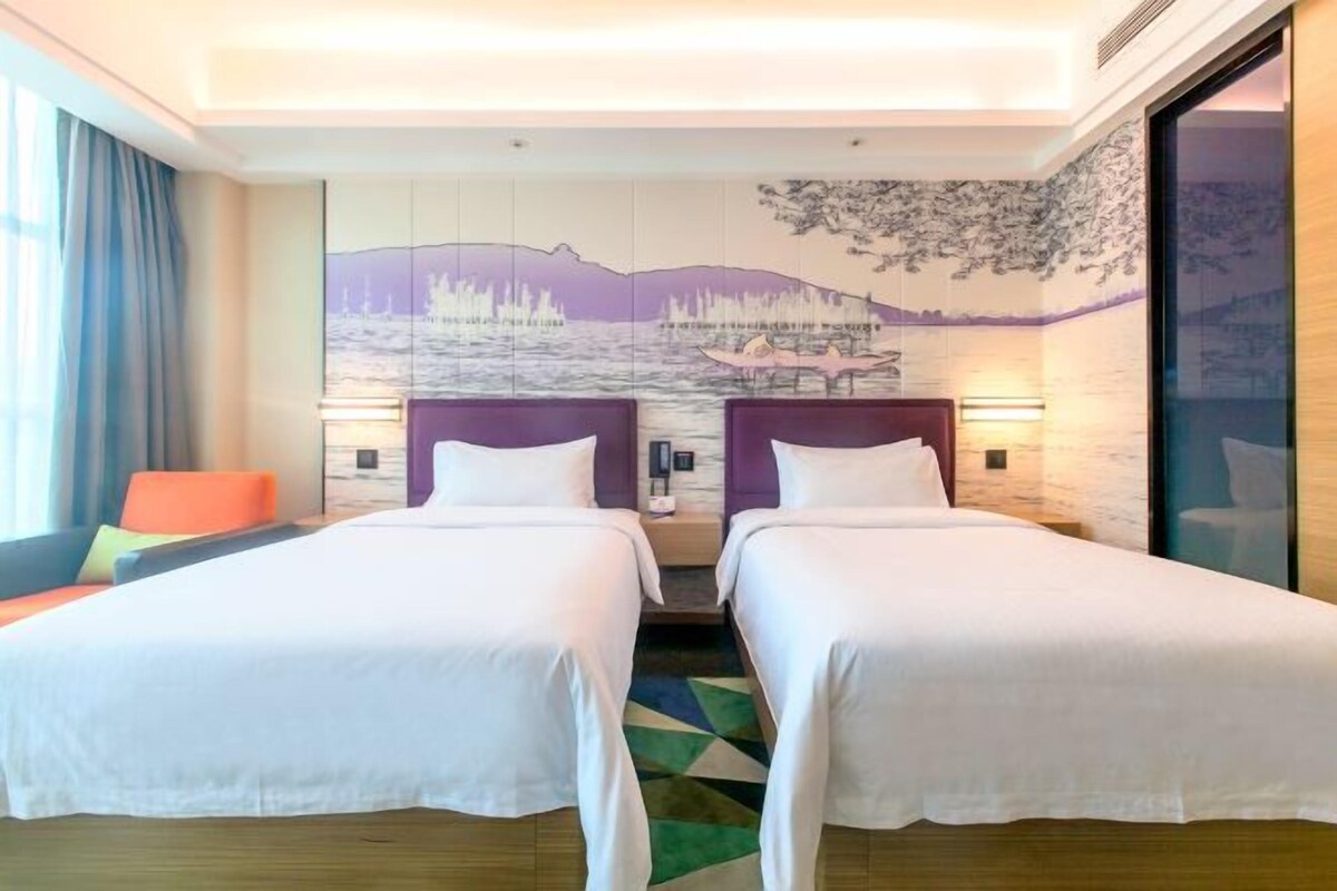 Habitación de hotel con dos camas, un ventanal con cortinas, una alfombra colorida y un mural en la pared.