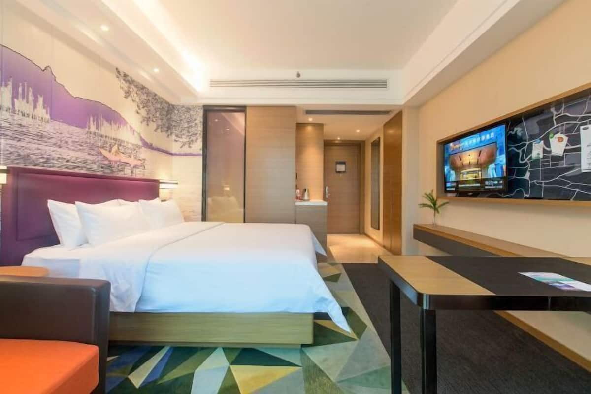 A hotel room with a bed, a desk, a television, and a mural on the wall.