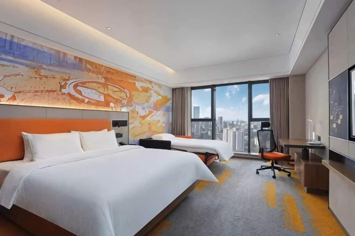 A hotel room with a large bed, a desk, a chair, and a city view.